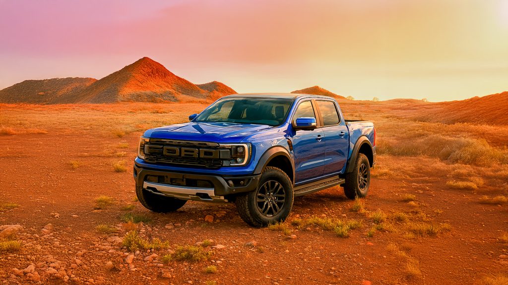 A blue Ford Ranger Raptor parked on a dusty red outback landscape under a vibrant sunset sky.